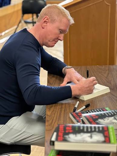 Red Shea signing books at a table.